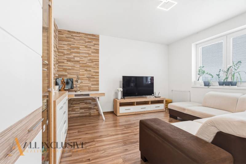 Obývací pokoj s podlahou s dřevěným dekorem, TV a krémovou sedačkou v 2pokojovém bytě.