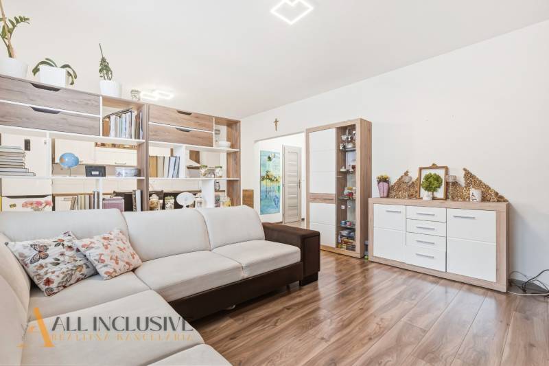 Obývací pokoj dvoupokojového bytu s béžovou sedačkou a podlahou s dřevěným dekorem.