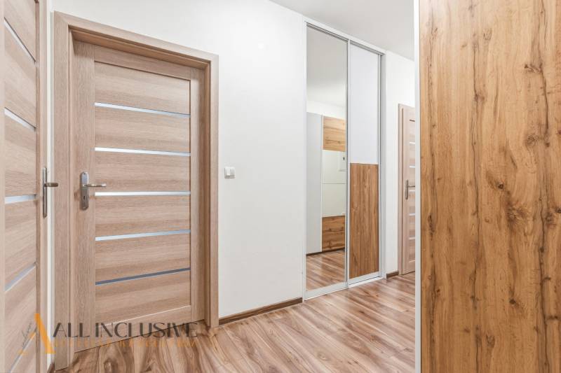 Chodba v 2-pokojovém bytě s podlahou s dřevěným dekorem a zrcadlovou skříní.