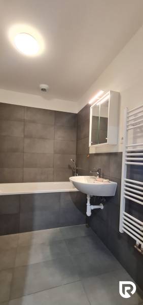 Koupelna v 2-pokojovém bytě s vanou, umyvadlem a zrcadlovou skříňkou.