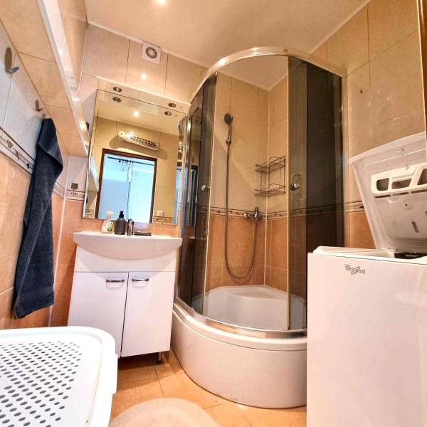 Koupelna v 2-pokojovém bytě se zaskleným sprchovým koutem a pračkou.