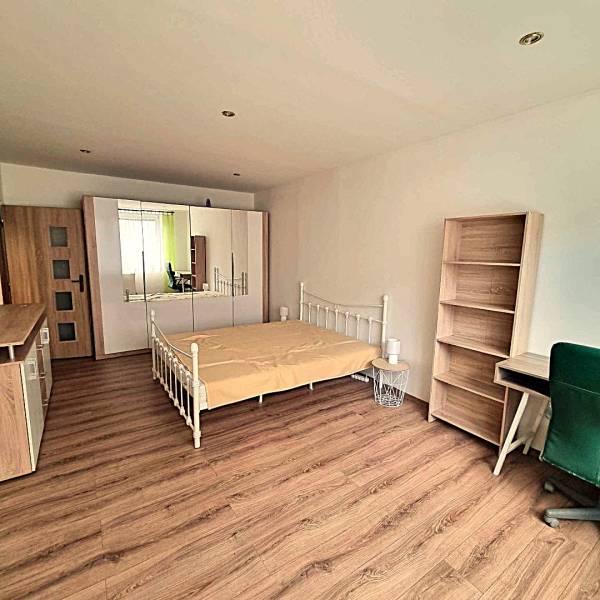 Ložnice v 2pokojovém bytě s postelí, skříní a podlahou s dřevěným dekorem.