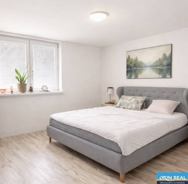 Světlá ložnice v rodinném domě s manželskou postelí a podlahou s dřevěným dekorem.