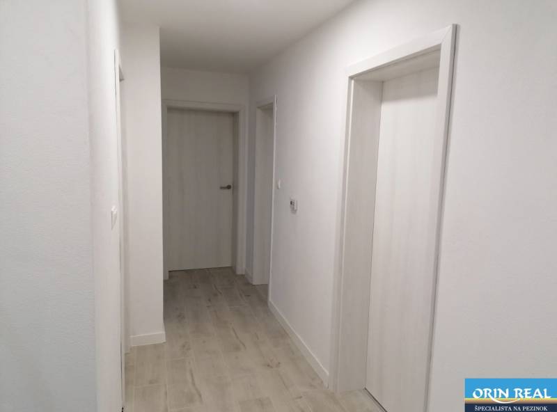 Chodba v rodinném domě s bílými stěnami a podlahou s dřevěným dekorem.