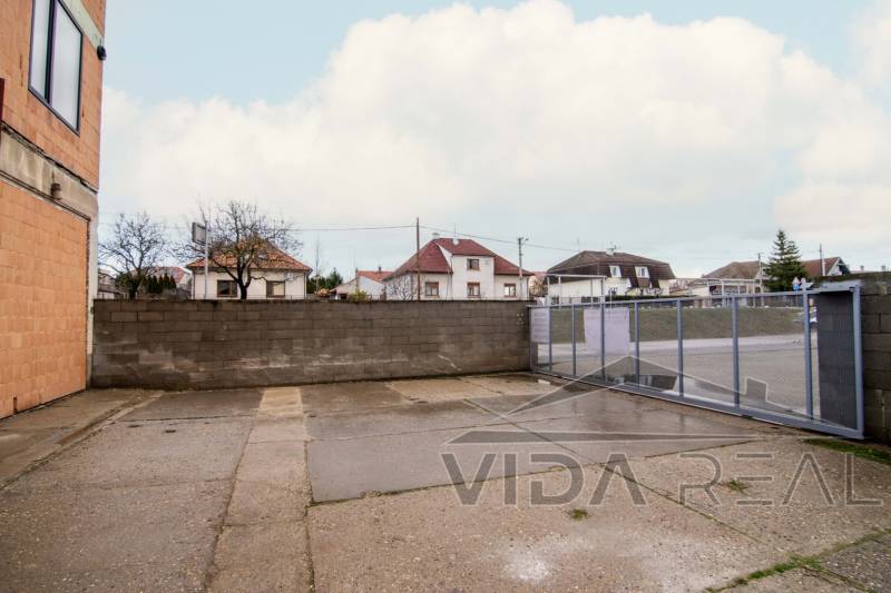 Exteriér na Nádražní ulici v Šenkvicích, vedle skladů a hal s ocelovou bránou.