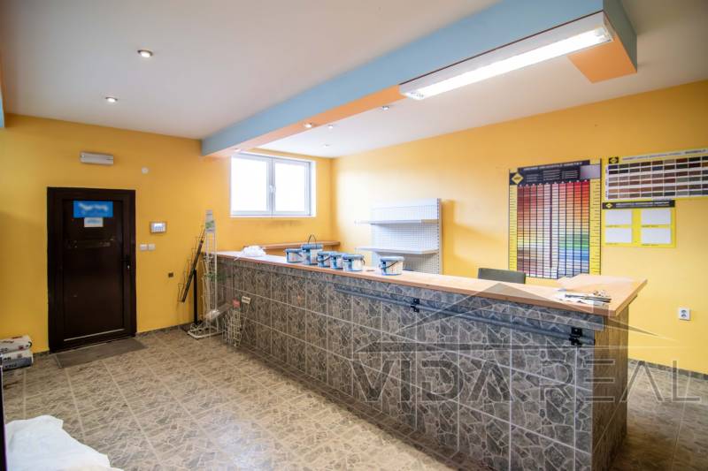 Interiér prodejny ve skladech a halách s pultem, poličkami a barevnými vzorky na stěně.