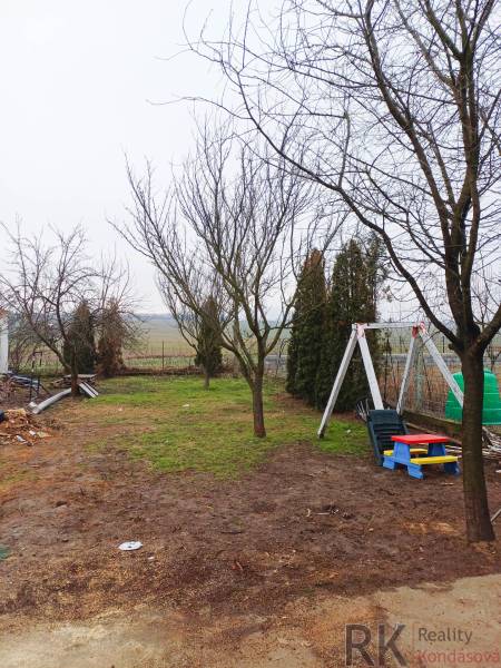 Zahrada rodinného domu ve Vizsoly se stromy a dětskou houpačkou na trávníku.