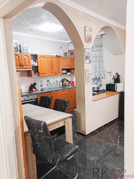 Kuchyně v rodinném domě s obloukovým vstupem, dřevěné skříňky a černé podlahy.