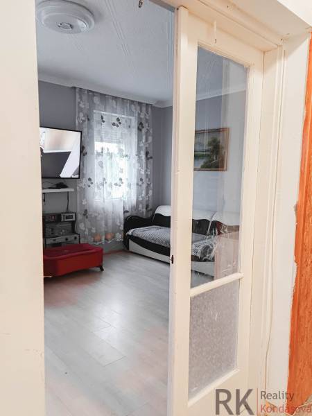 Obývací pokoj v rodinném domě s televizí a podlahou s dřevěným dekorem.