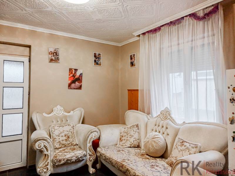 Obývací pokoj rodinného domu s ornamentálním nábytkem a fotografiemi na stěnách.