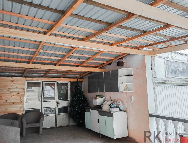 Rodinný dům: Přístřešek s kovovou střechou, ratanová křesla, umělé stromky, úložné prostory.