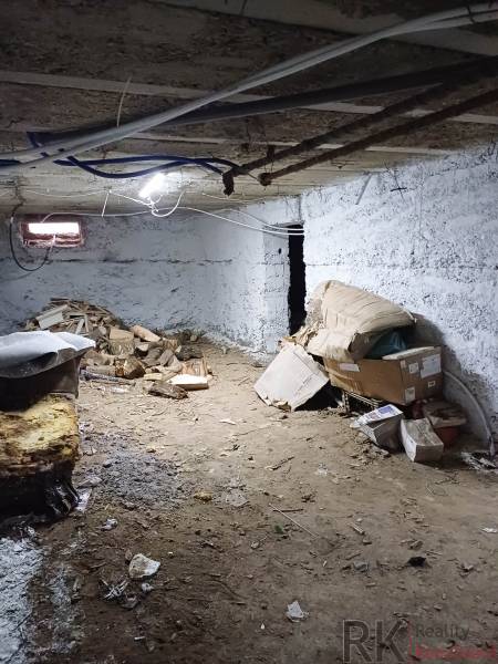 Suterén rodinného domu s hliněnou podlahou, několika krabicemi a dřevem.