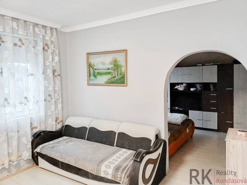 Světlý obývací pokoj s pohovkou, velkým obloukovým průchodem a závěsy s květinovým vzorem.