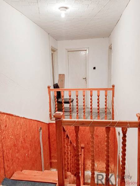 Schodiště s dřevěným zábradlím v rodinném domě, bílé stěny, osvětlení se žárovkou.