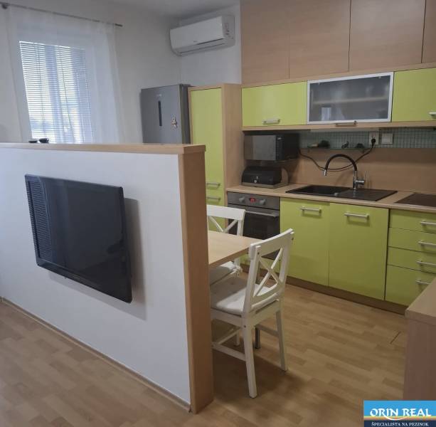 Kuchyně v 2-pokojovém bytě se zelenými skříňkami, televizorem a stolem se dvěma židlemi.