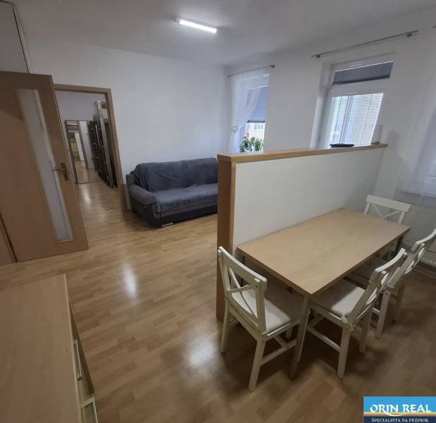 Interiér s pohovkou, jídelním stolem a podlahou s dřevěným dekorem v 2-pokojovém bytě.