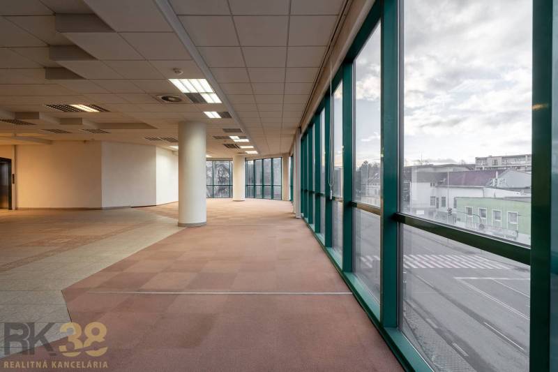 Prostorné kanceláře s velkými okny a rozložitými sloupy, výhled na ulici.
