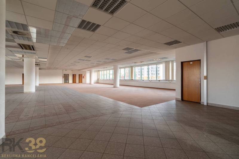Prostorné kanceláře s okny, podlahou s dřevěným dekorem a sloupy.