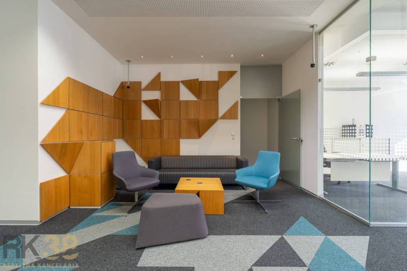 Interiér kanceláří s barevným sezením, sklem a geometrickými dřevěnými panely.