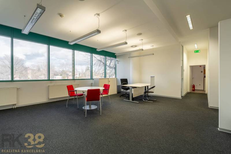 Kanceláře s černým kobercem, červenými židlemi a velkými okny v přízemí.