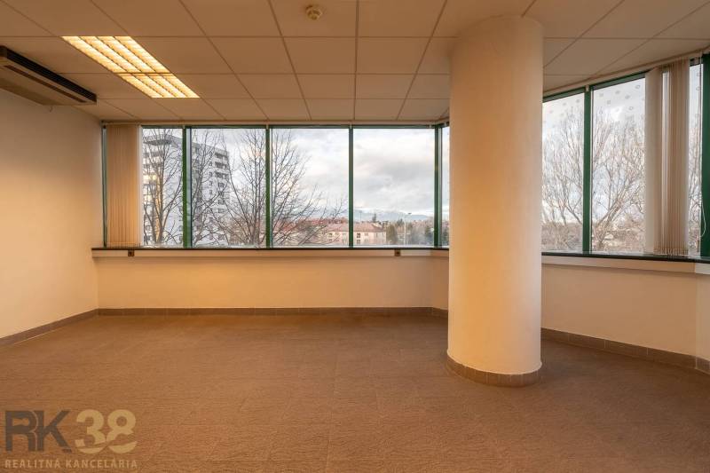 Interiér kanceláří s velkými okny a sloupem, podlaha s dřevěným dekorem.