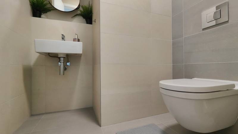 Koupelna dvoupokojového bytu se závěsnou toaletou, umyvadlem a bílými dlaždicemi.