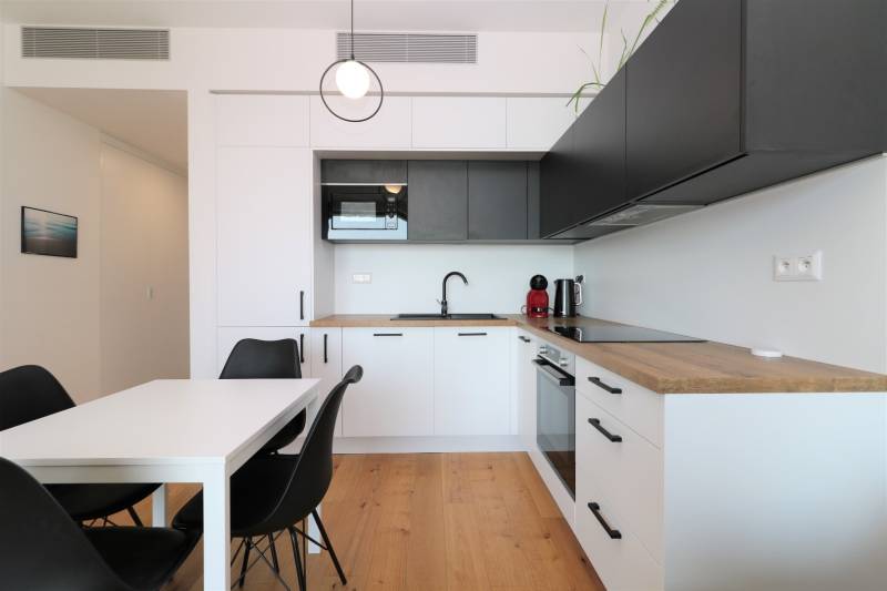 Kuchyně v 2-pokojovém bytě s podlahou s dřevěným dekorem a černými skříňkami.