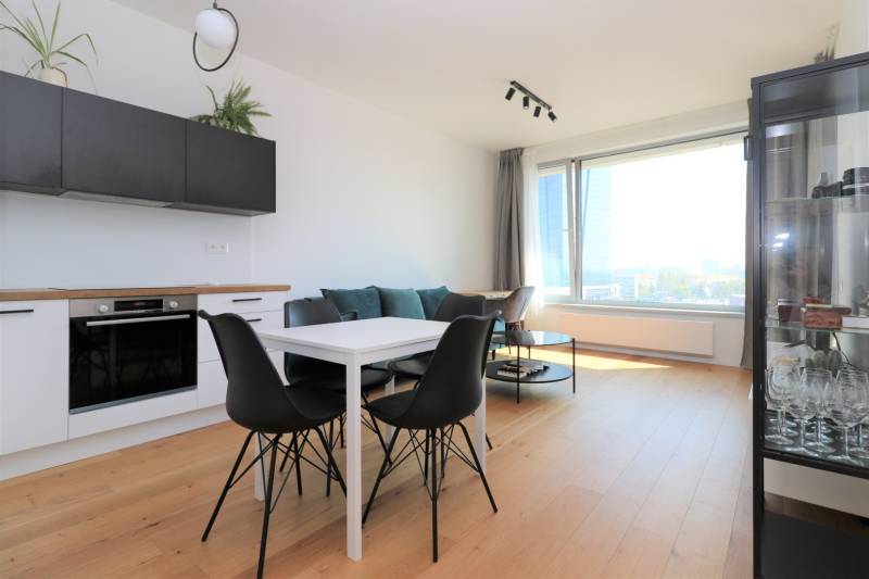 Kuchyně a jídelní stůl s černými židlemi v dvoupokojovém bytě s podlahou s dřevěným dekorem.