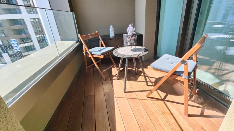 Balkon s podlahou s dřevěným dekorem, posezení a okrasný stůl v 2-pokojovém bytě.