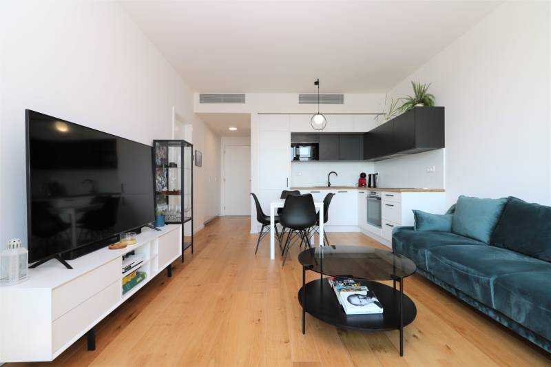 Obývací pokoj s kuchyní v 2pokojovém bytě, podlaha s dřevěným dekorem, TV a sedací souprava.