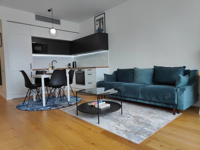 Obývací pokoj s kuchyňským koutem, tyrkysovou sedačkou, dřevěným dekorem a jídelním stolem.