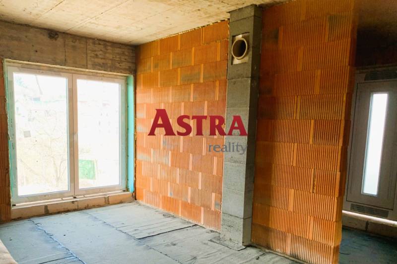 Nedokončený interiér budovy se surovými cihlami a velkými okny přináší potenciál útulné chaty.