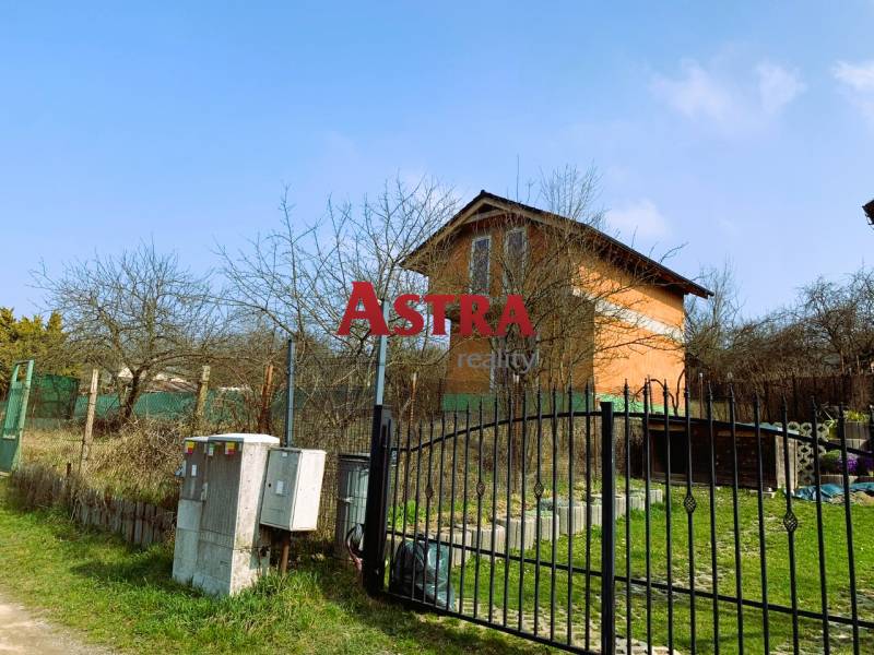 Na obrázku je chata obklopená stromy a plotem na travnatém pozemku.