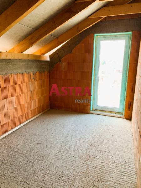 Podkrovní pokoj s cihlovými stěnami, dřevěnými trámy a světlem prosvětlená chata.