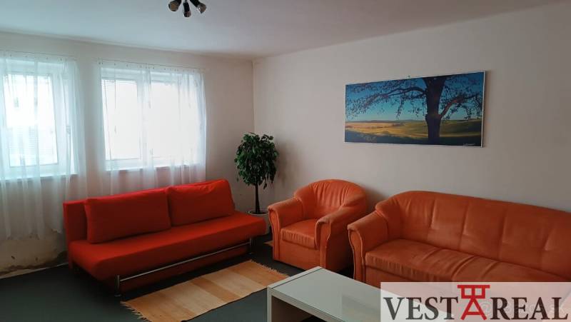 Obývací pokoj v rodinném domě s oranžovou sedačkou, křesly a obrazem krajiny.