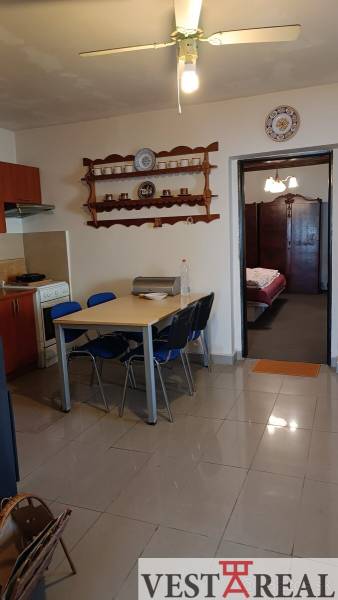 Jídelní stůl se židlemi v rodinném domě, kuchyňská část a otevřené dveře do ložnice.