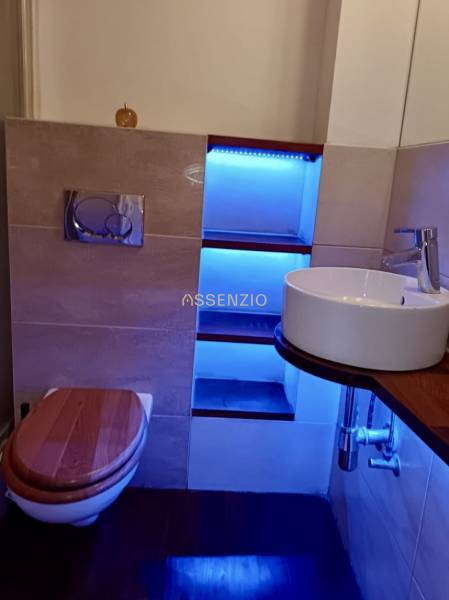 Koupelna ve 3-pokojovém bytě se závěsným WC, umyvadlem, podsvícenou policí a dřevěným dekorem.