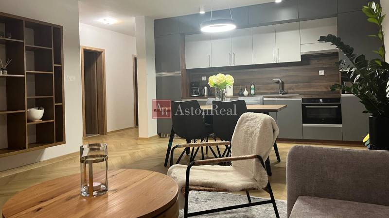 Obývací pokoj v třípokojovém bytě s kuchyní, stolem a podlahou s dřevěným dekorem.