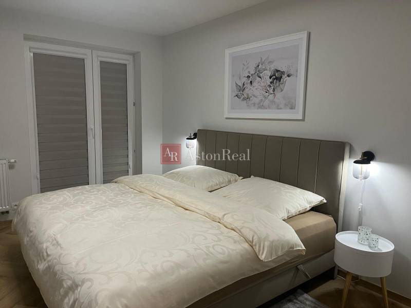 Ložnice v 3-pokojovém bytě se světlou postelí a jemným dekorem na stěně.