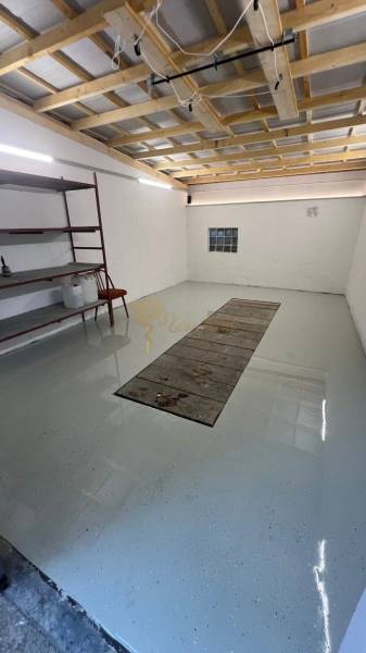 Garáže s regály a světlými stěnami, podlaha s jámou na opravu vozidel.