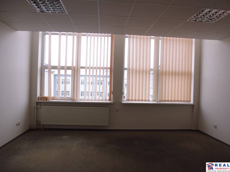 Kancelář s velkým oknem, žaluziemi a podlahou s dřevěným dekorem.