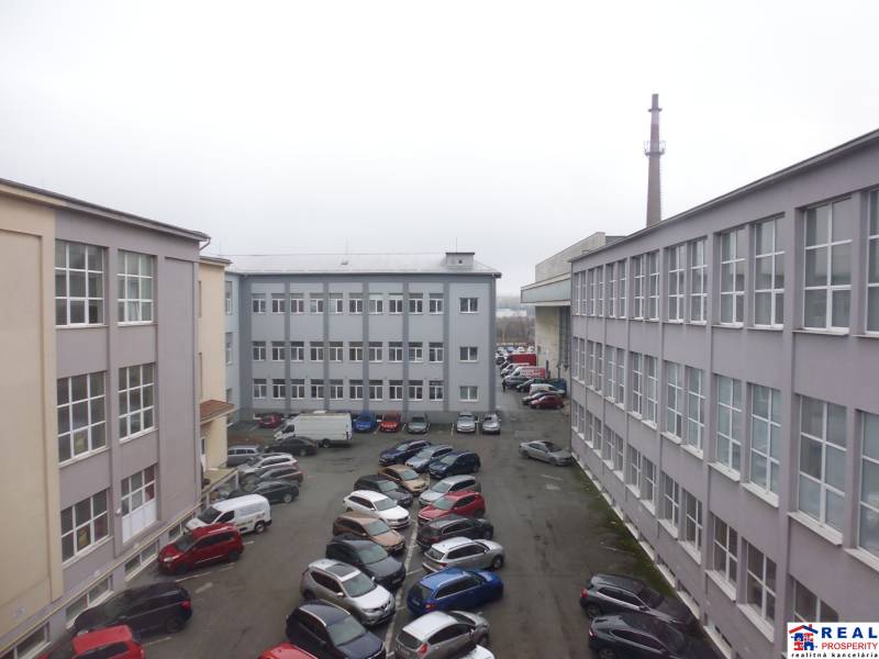 Budovy kanceláří na Masarykově ulici v Prešově s množstvím zaparkovaných aut na dvoře.