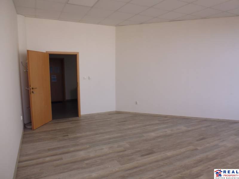 V kanceláři s podlahou s dřevěným dekorem jsou bílé stěny a otevřené dveře.