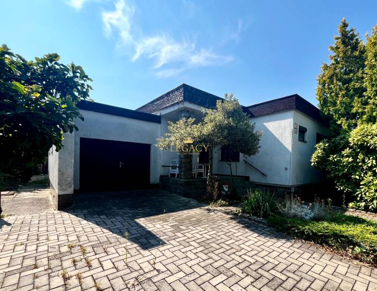 Rodinný dům v Ivance pri Dunaji s garáží a květinovým záhonem, na dlážděném chodníku.