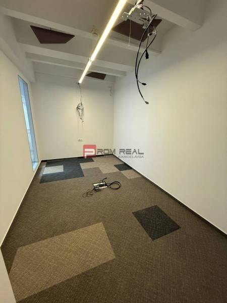 Kanceláře s barevným kobercem, bílé stěny, kabely ze stropu.