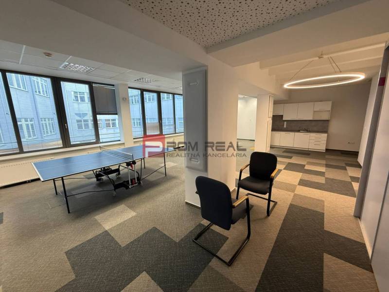 Kanceláře se stolním tenisem, posezením a kuchyňkou na podlaze s dřevěným dekorem.