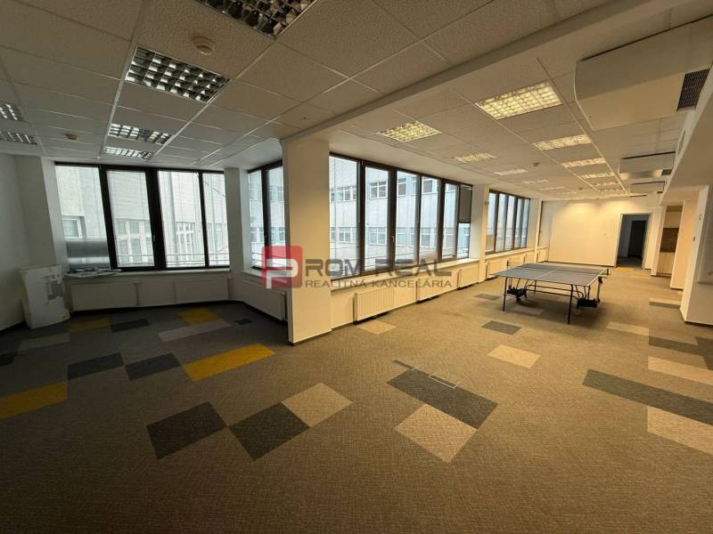 Kanceláře s velkými okny a kobercovou podlahou, místnost obsahuje pingpongový stůl.