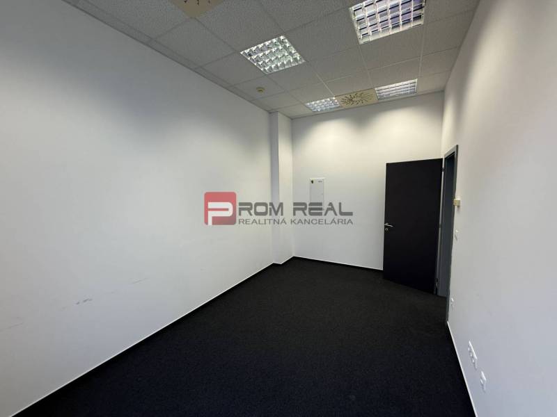 Kanceláře s bílými stěnami a tmavým kobercem.