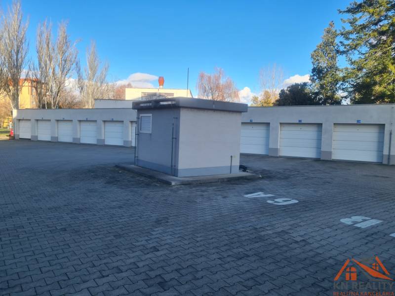 Řadová garáž v Komárně s uzavřenými branami na zpevněném povrchu za slunečného počasí.