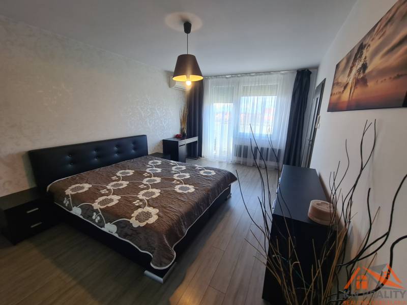 Ložnice v dvoupokojovém bytě s postelí, skříňkou a podlahou s dřevěným dekorem.